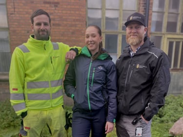 Tre Sekomedlemmar som tittar in i kameran. Två män och en kvinna, de står iklädda arbetskläder från sina företag där de jobbar.