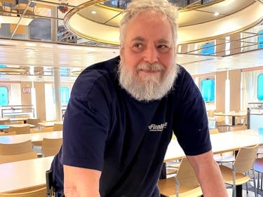 Man med vitt skägg och arbetskläder lutar sig över ett bord i en konferenslokal.